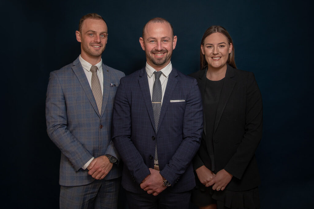 A team photo for Mike Murphy Bayleys Pukekohe real estate of three team members smiling at the camera on a dark blue background