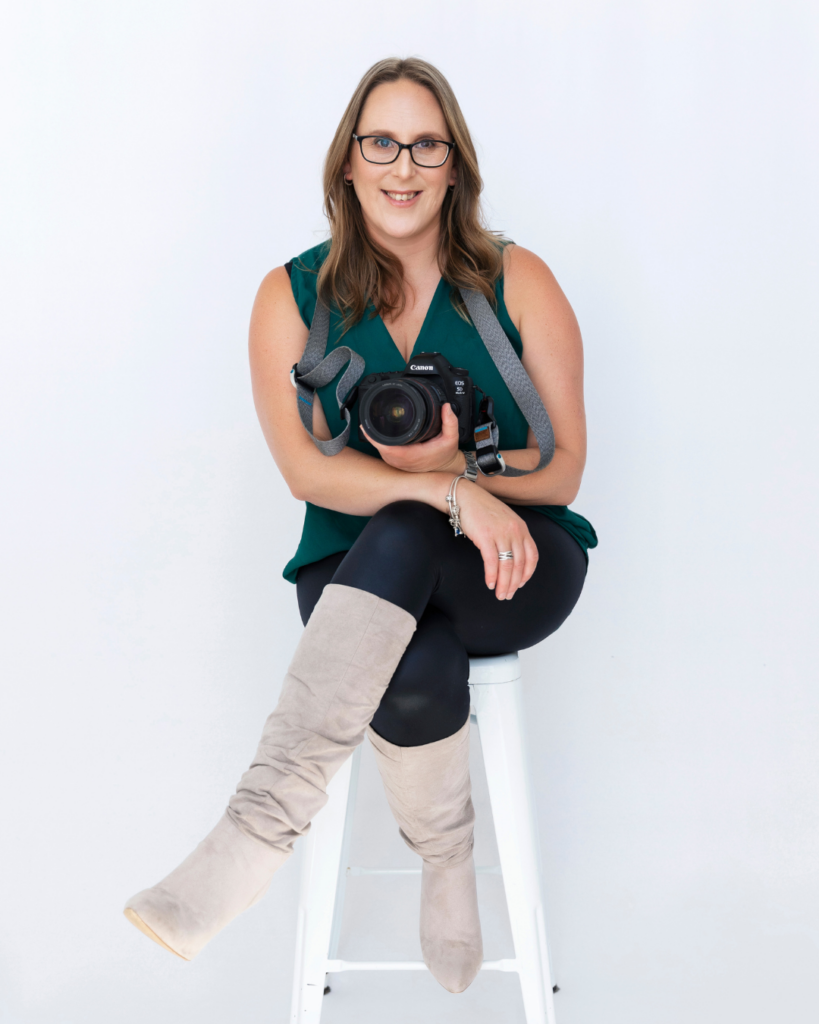 photo of Katrina Johns sitting on white stool holding her camera and looking directly at the viewer. Social Shoots branding photographer